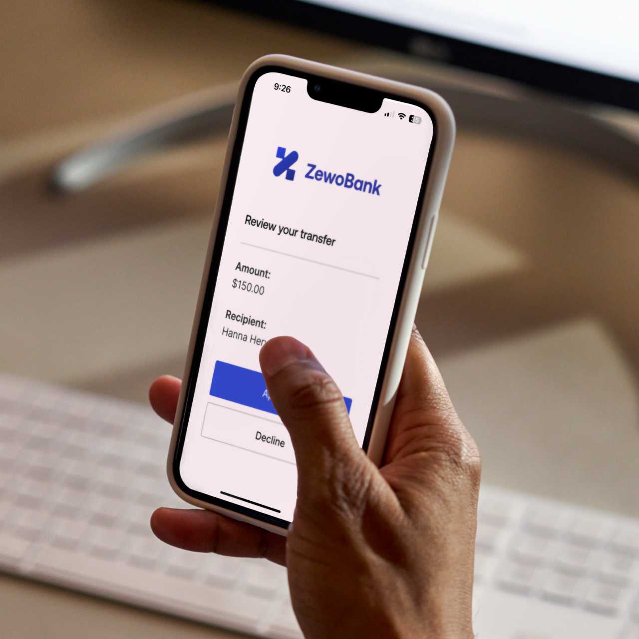Hand holding a smartphone that's displaying a review your money transfer request from ZewoBank.