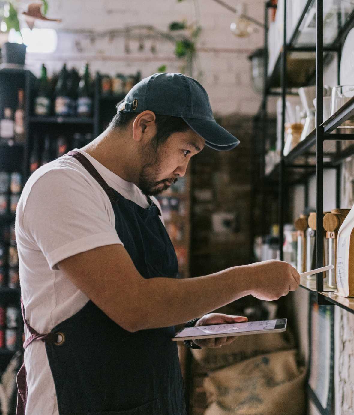 A man wearing an apron and a hat taking inventory of packaged goods in a retail shop